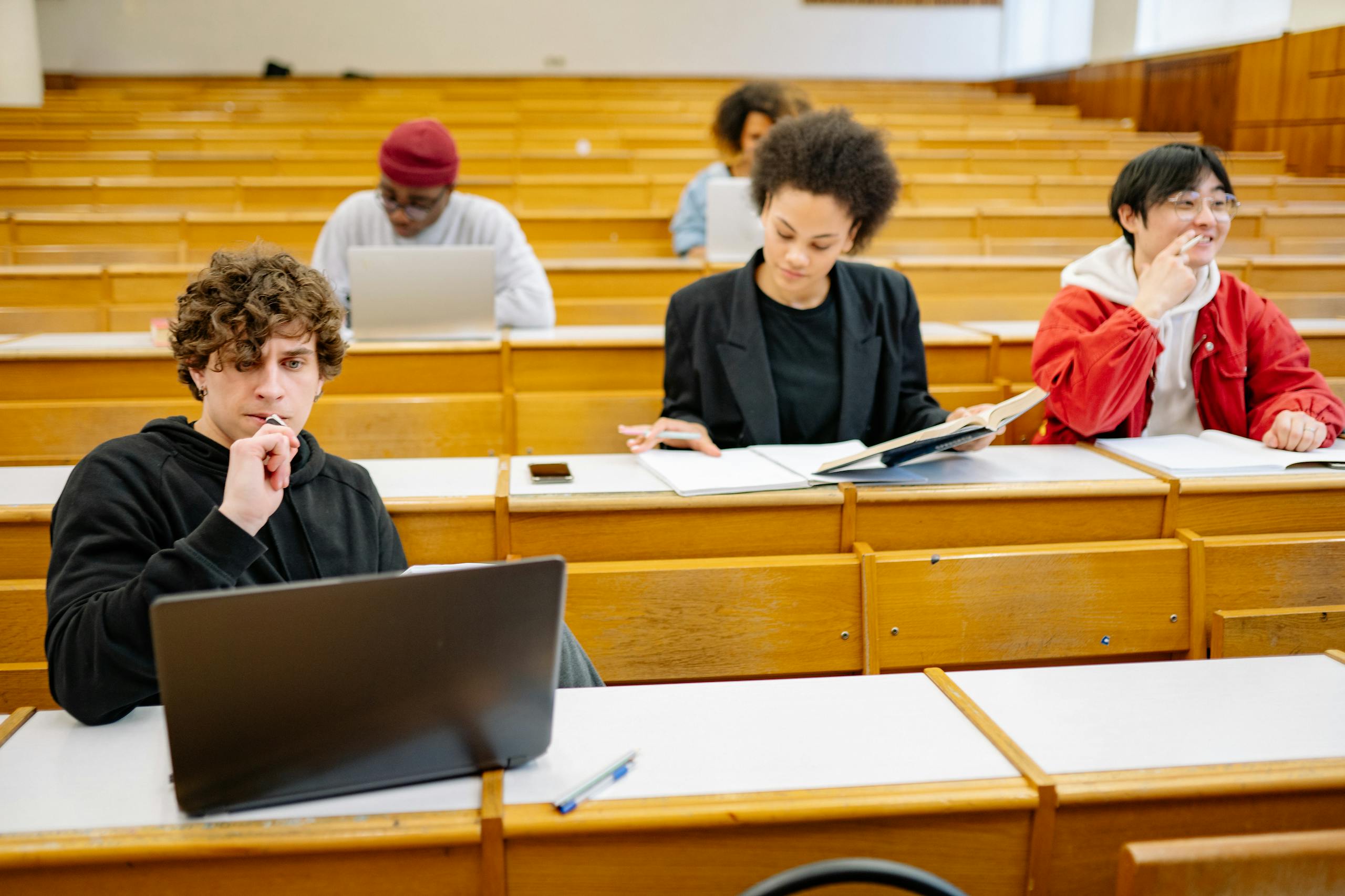 A diverse group of hospitality students studying in a classroom setting with laptops and books.
