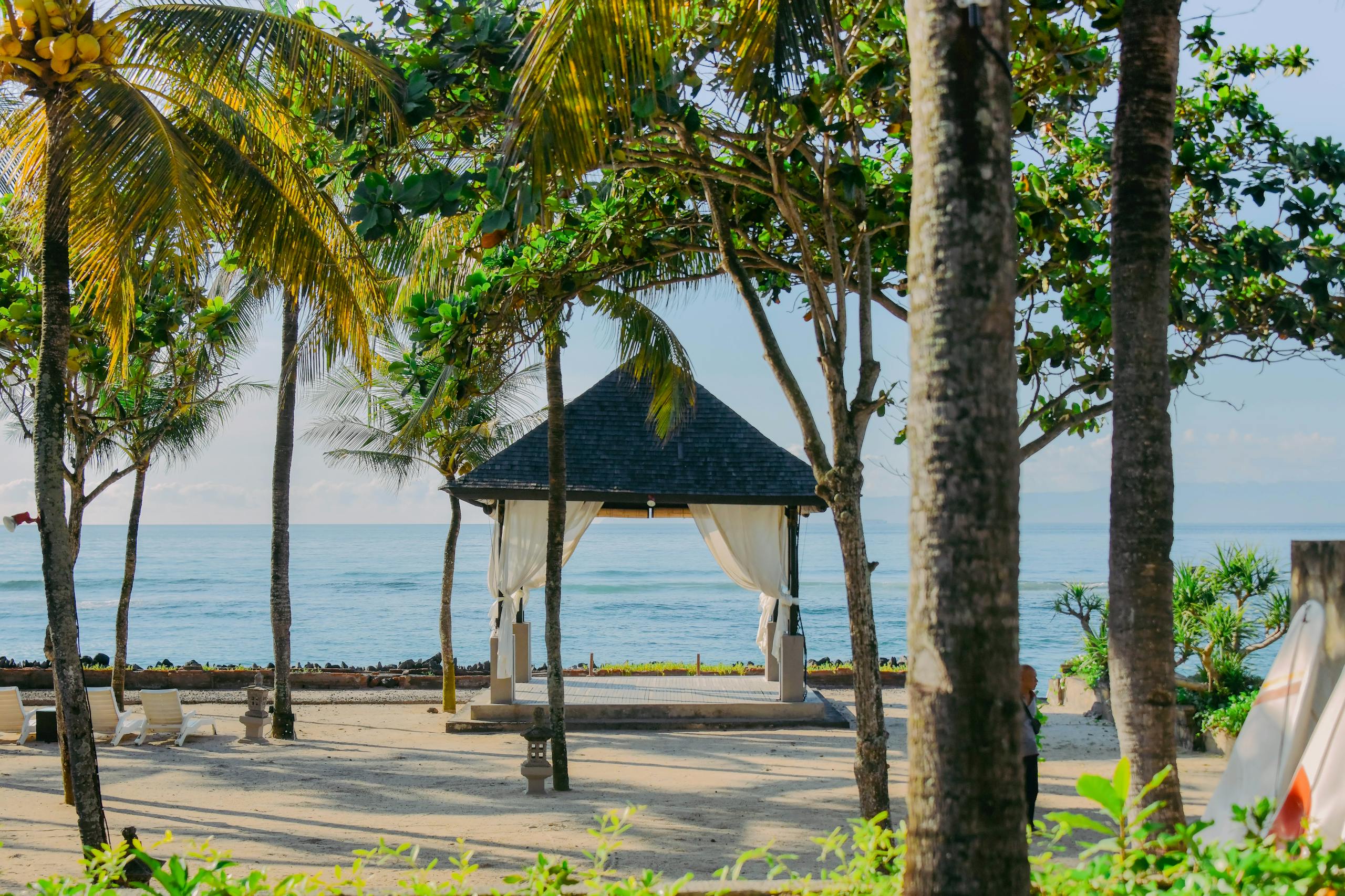 Tropical pavilion with palm trees by the beach in Bali, Indonesian, offering a serene coastal view.
