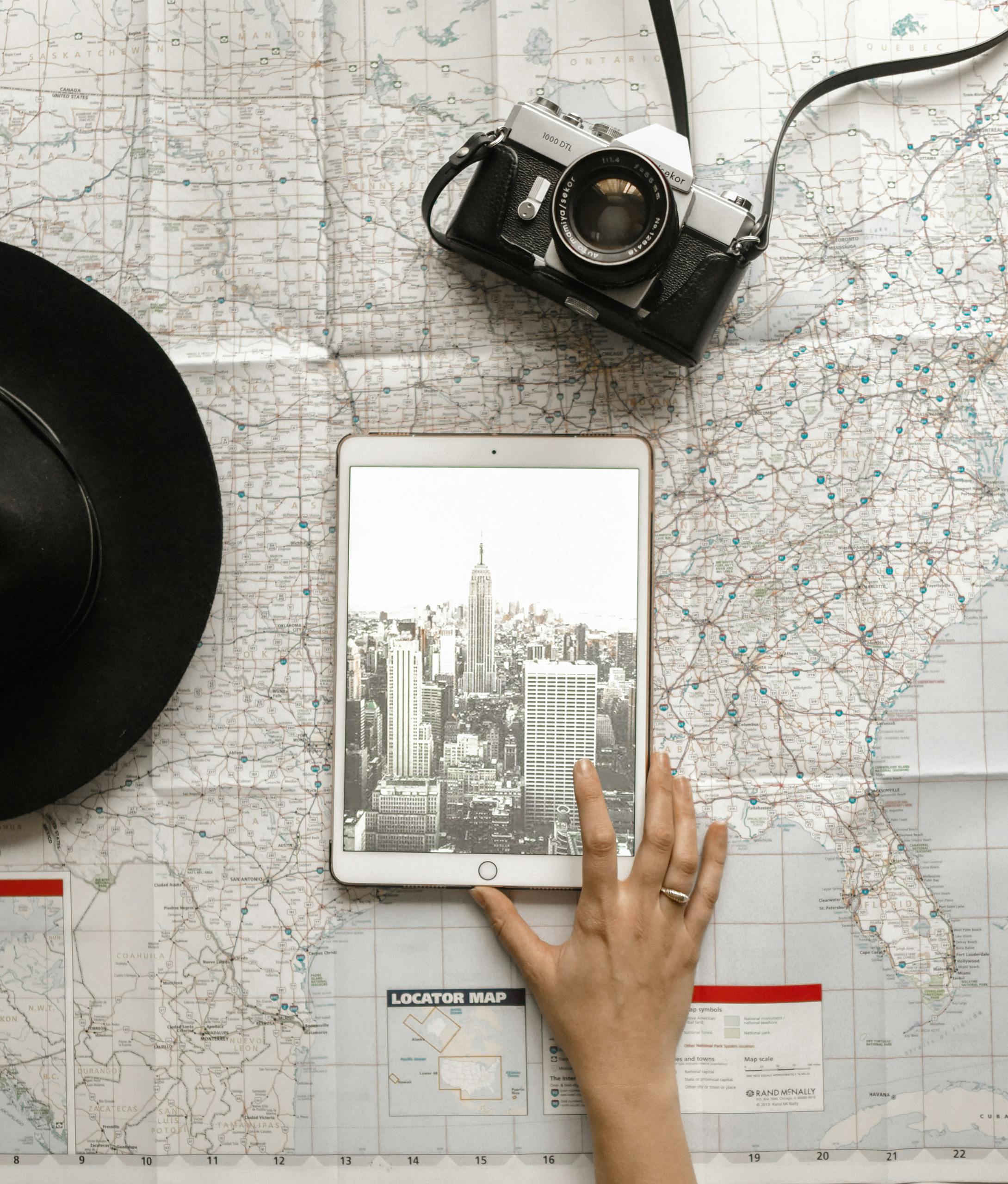 Flat lay of vintage camera, iPad with New York City skyline, and a hand on a map, AI travel planning