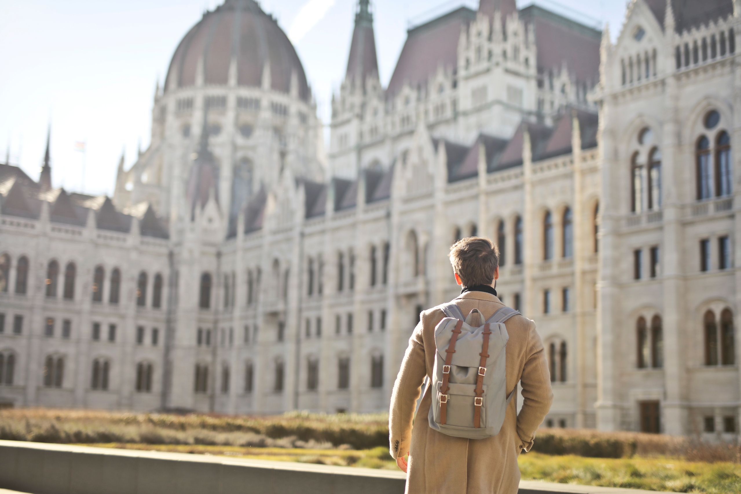 A student traveling europe admires the grandeur of the Hungarian Parliament Building in Budapest during daylight.