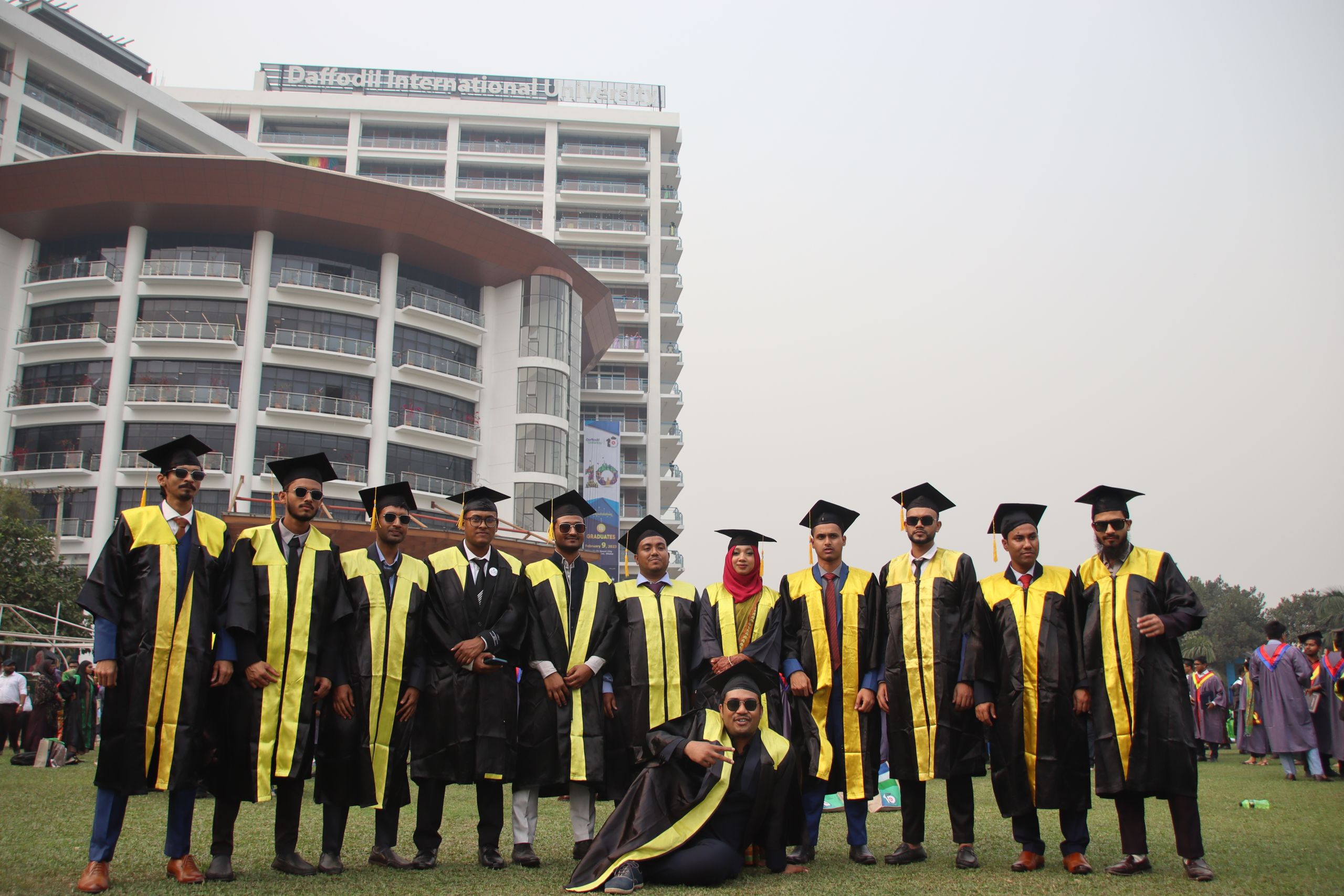 Graduating DBA students celebrating with friends in front of university building.